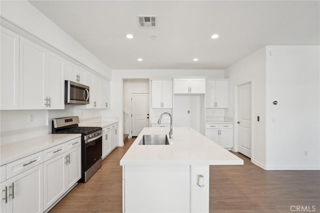 kitchen featuring visible vents, an island with sink, a sink, stainless steel appliances, and white cabinets