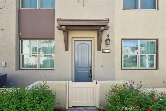 view of exterior entry with a gate, stucco siding, and fence