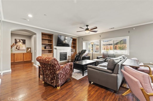 living area with visible vents, dark wood-type flooring, a ceiling fan, arched walkways, and a fireplace