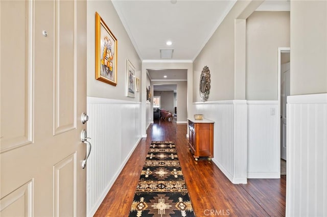 hallway featuring a wainscoted wall, visible vents, dark wood finished floors, and crown molding