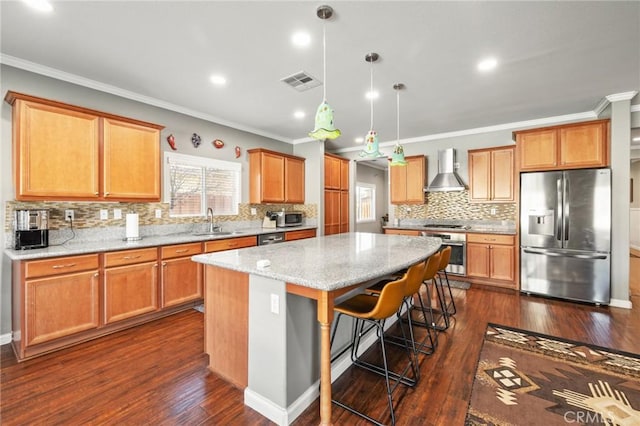 kitchen featuring visible vents, a sink, a kitchen island, stainless steel appliances, and wall chimney range hood