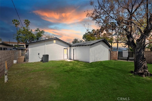 back of property at dusk featuring central AC unit, a yard, a fenced backyard, and stucco siding