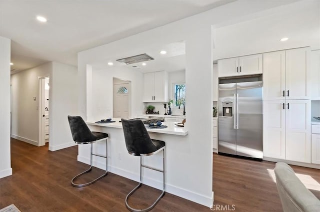 kitchen featuring stainless steel fridge with ice dispenser, dark wood finished floors, light countertops, a kitchen breakfast bar, and white cabinetry