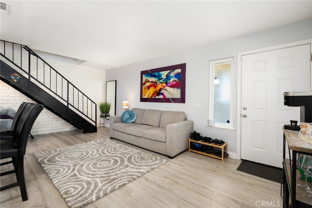 living area with visible vents, brick wall, wood finished floors, and stairs