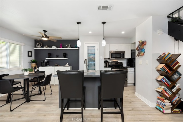 kitchen featuring stainless steel microwave, visible vents, light wood-style floors, white cabinets, and range