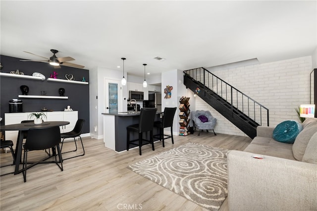 interior space featuring stairway, a ceiling fan, visible vents, brick wall, and light wood-style flooring