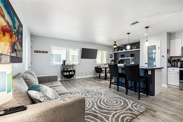 living area featuring light wood finished floors, visible vents, a ceiling fan, and baseboards