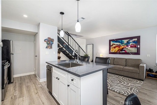 kitchen featuring dark countertops, light wood finished floors, appliances with stainless steel finishes, white cabinets, and a sink