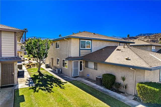 back of house featuring stucco siding, a lawn, roof with shingles, and cooling unit