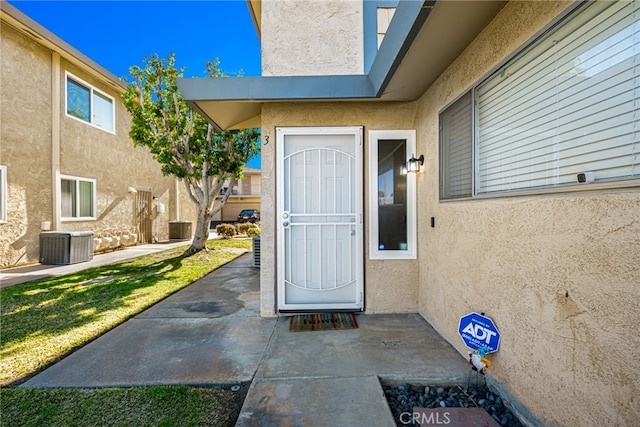 entrance to property featuring stucco siding, central air condition unit, and a patio area