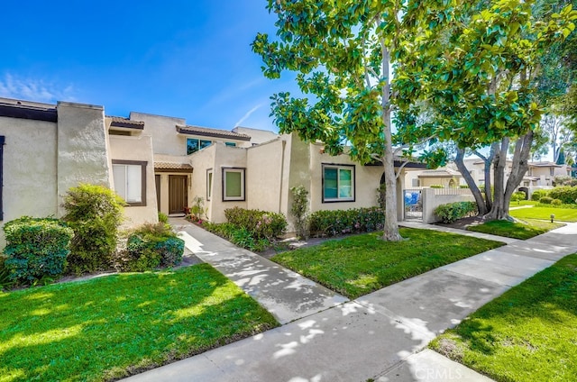 view of property featuring a front yard, fence, a tile roof, and stucco siding