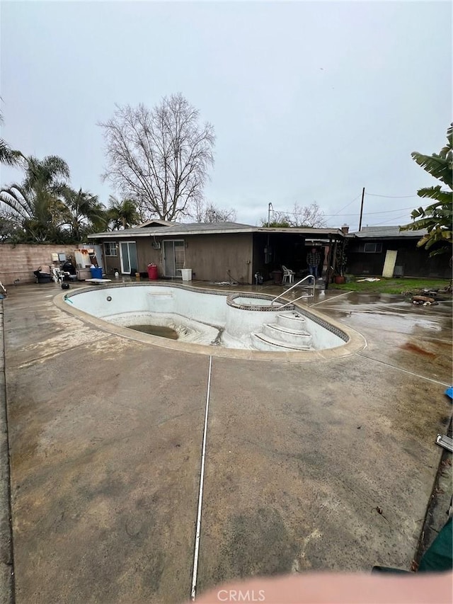 rear view of house with an in ground hot tub, a patio area, and an empty pool