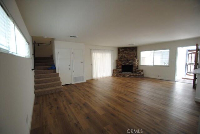 unfurnished living room with visible vents, a fireplace, stairs, and wood finished floors