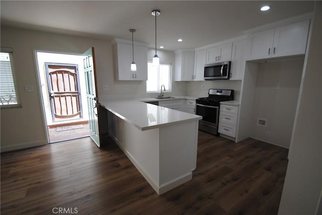 kitchen featuring a sink, dark wood finished floors, stainless steel appliances, a peninsula, and white cabinets