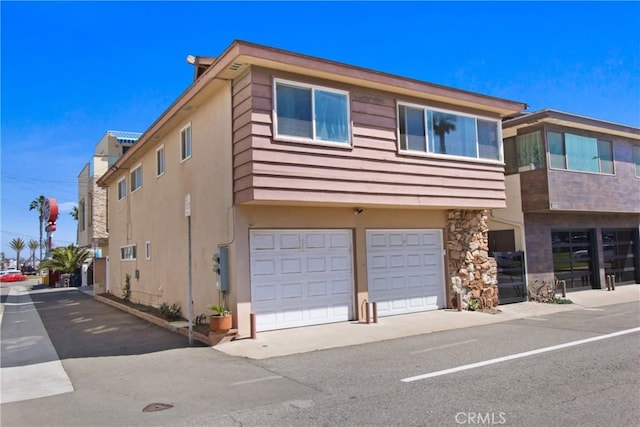 view of front of home featuring an attached garage, stone siding, and stucco siding