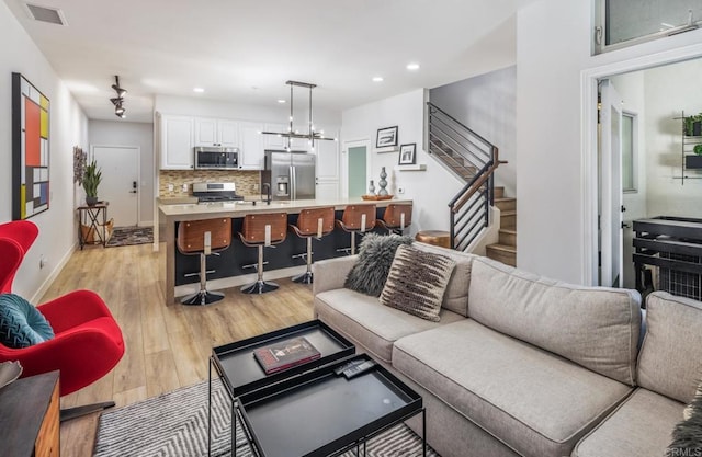 living room with stairway, visible vents, light wood finished floors, baseboards, and recessed lighting