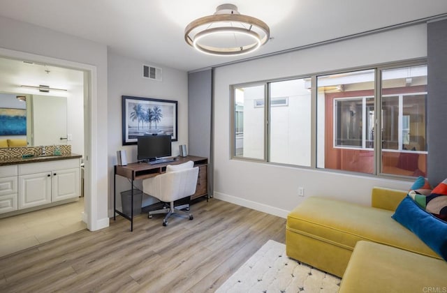 home office with a sink, visible vents, baseboards, and light wood finished floors