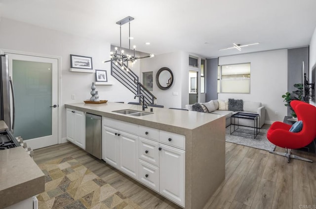 kitchen featuring dishwasher, light countertops, a peninsula, white cabinets, and a sink