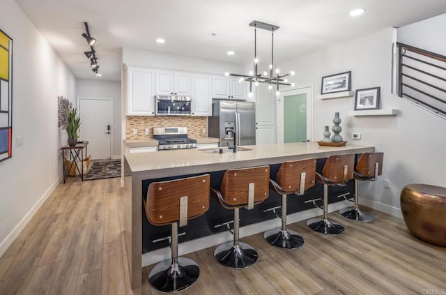 kitchen featuring light wood finished floors, backsplash, a breakfast bar, appliances with stainless steel finishes, and white cabinetry