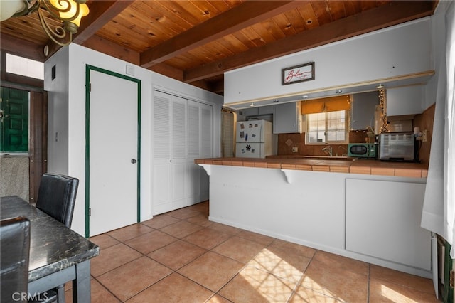 kitchen featuring tile countertops, light tile patterned flooring, freestanding refrigerator, beamed ceiling, and tasteful backsplash