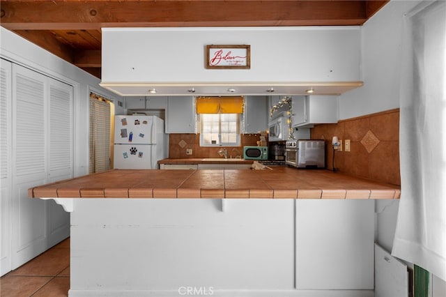 kitchen with white appliances, a peninsula, light tile patterned flooring, tile counters, and tasteful backsplash