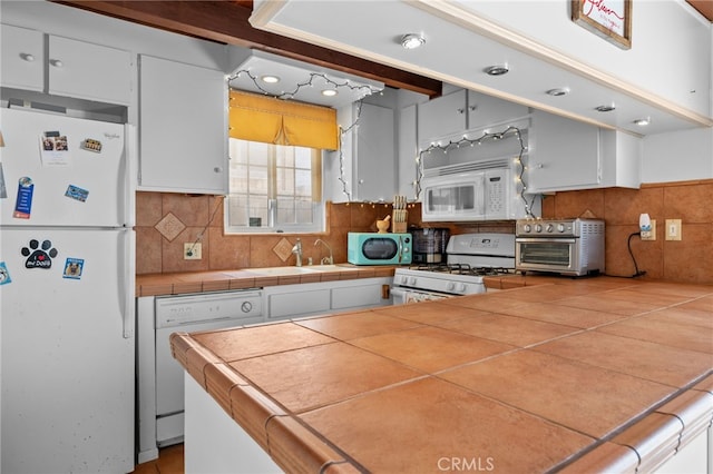 kitchen with tasteful backsplash, a toaster, tile countertops, white cabinets, and white appliances