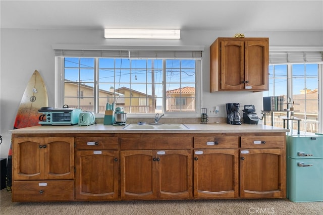 kitchen featuring light countertops, a healthy amount of sunlight, brown cabinets, and a sink