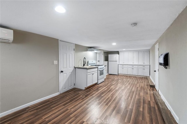 kitchen featuring dark wood finished floors, white appliances, a wall unit AC, and baseboards