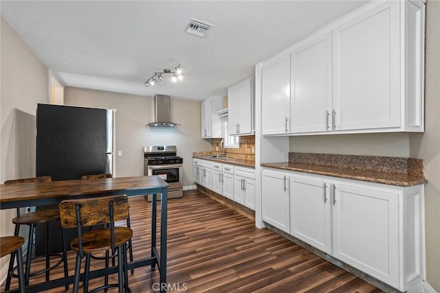 kitchen with visible vents, a sink, white cabinets, appliances with stainless steel finishes, and wall chimney range hood