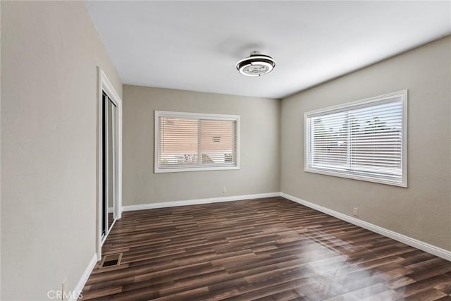 unfurnished room with visible vents, baseboards, and dark wood-style flooring