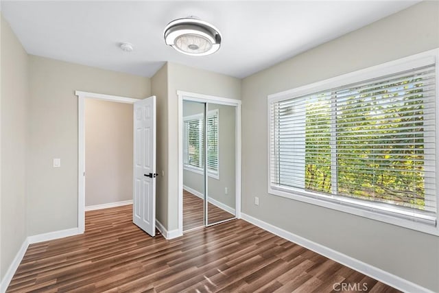 unfurnished bedroom with a closet, baseboards, and dark wood-style flooring