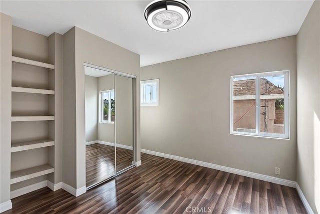 unfurnished bedroom featuring baseboards, multiple windows, a closet, and dark wood-style floors