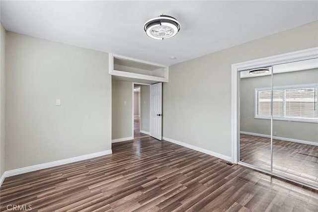 unfurnished bedroom featuring a closet, baseboards, and dark wood-type flooring