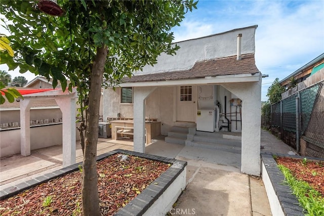 rear view of house with a patio area, stucco siding, entry steps, and fence