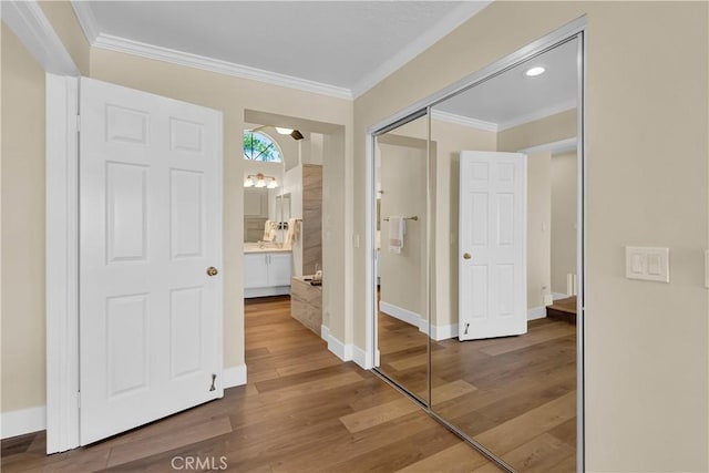 corridor featuring baseboards, arched walkways, wood finished floors, and crown molding