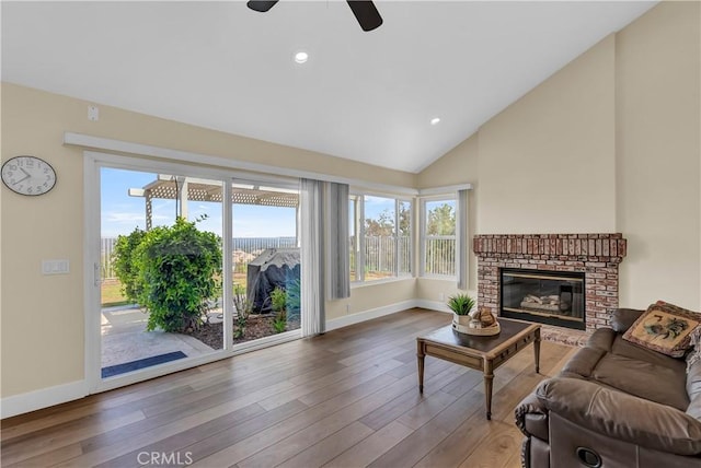 living room with vaulted ceiling, a brick fireplace, wood finished floors, and baseboards