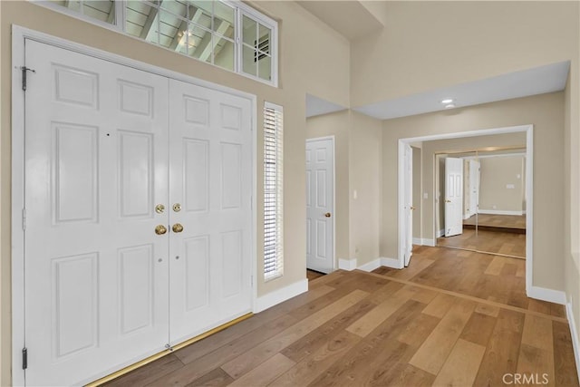 entrance foyer featuring light wood finished floors, a wealth of natural light, baseboards, and a towering ceiling