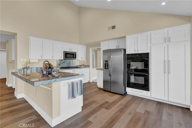 kitchen with visible vents, light wood-style floors, appliances with stainless steel finishes, a peninsula, and white cabinets