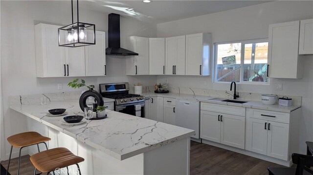 kitchen with a peninsula, stainless steel range with gas stovetop, white dishwasher, a sink, and wall chimney exhaust hood