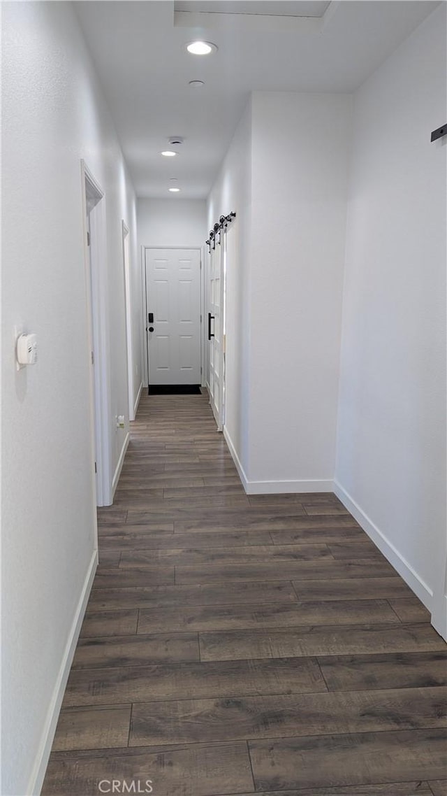 hall with dark wood finished floors, recessed lighting, baseboards, and a barn door