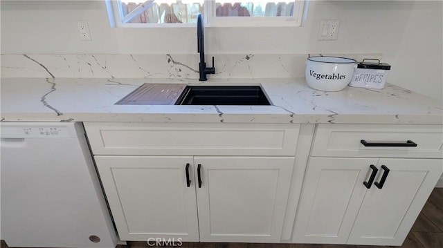 interior details featuring white cabinets, light stone countertops, white dishwasher, and a sink