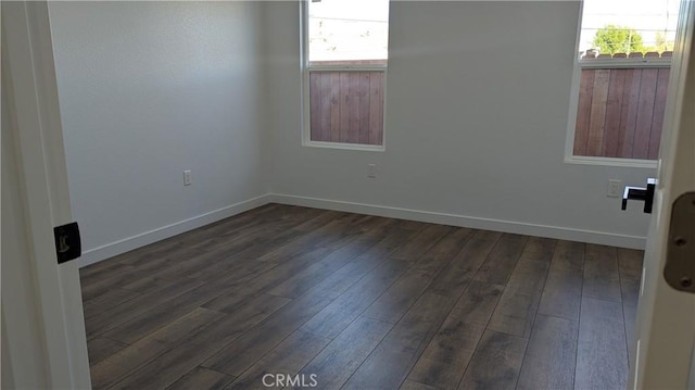 spare room featuring baseboards, a healthy amount of sunlight, and dark wood-style flooring