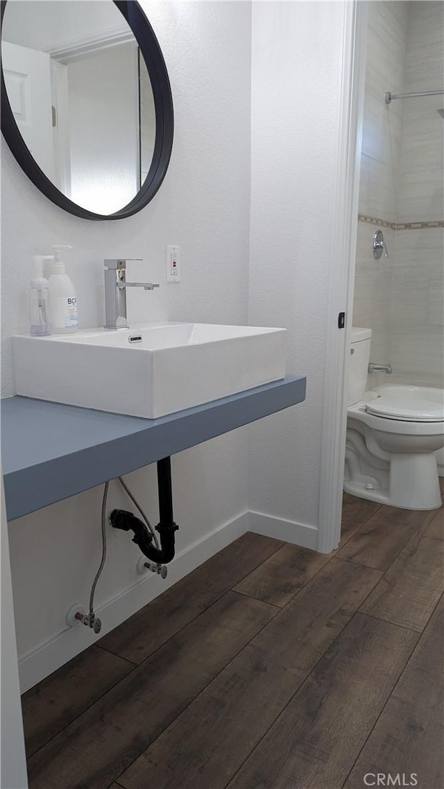 bathroom with baseboards, tiled shower, toilet, and wood finished floors