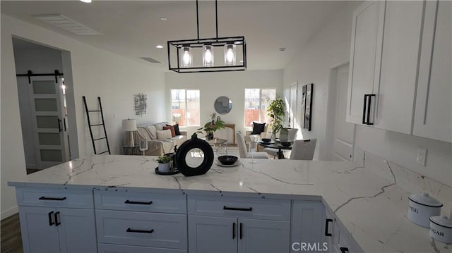 kitchen with visible vents, open floor plan, a barn door, a peninsula, and light stone countertops