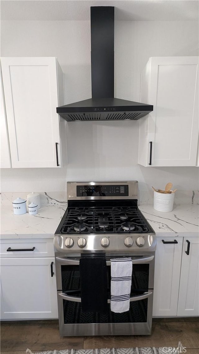 kitchen with range with two ovens, light stone counters, wall chimney exhaust hood, and white cabinets