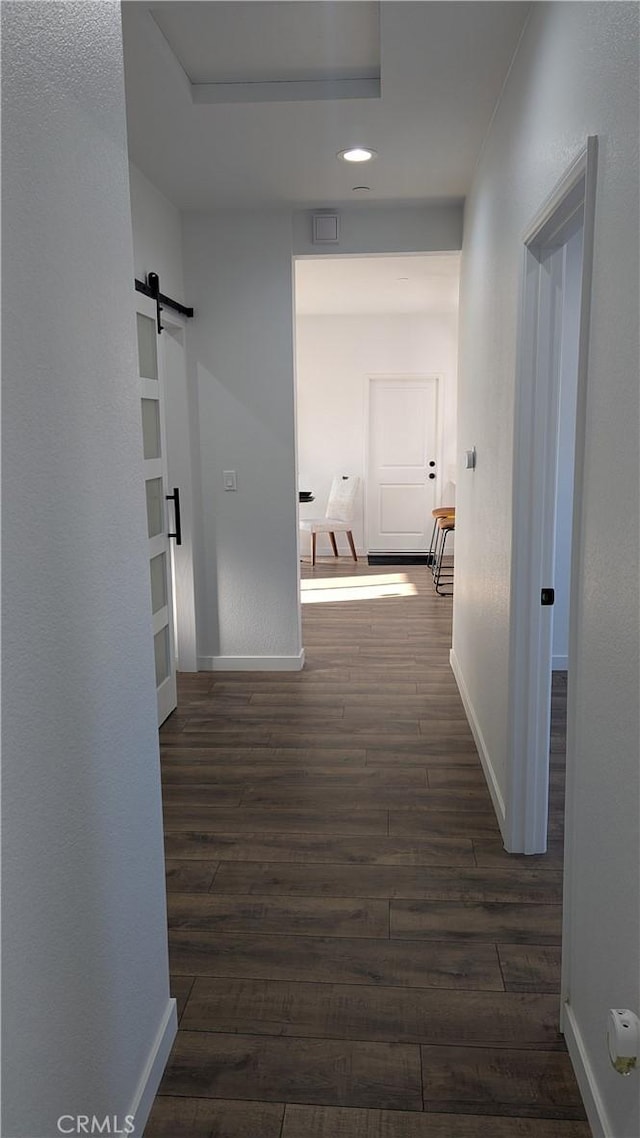 hallway featuring a barn door, baseboards, dark wood-type flooring, and visible vents