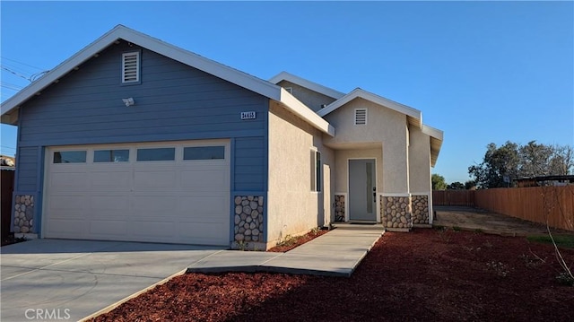 view of front of property with fence, driveway, an attached garage, stucco siding, and stone siding