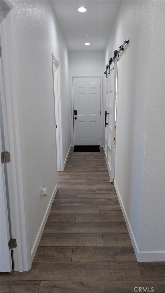 corridor with a barn door, recessed lighting, baseboards, and dark wood-type flooring