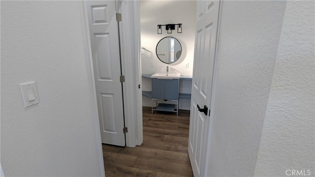 corridor with dark wood-style floors, a textured wall, and a sink