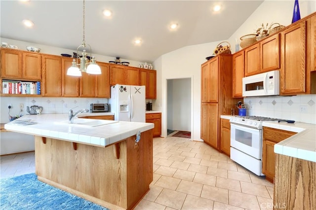 kitchen featuring white appliances, brown cabinetry, lofted ceiling, a sink, and tile counters